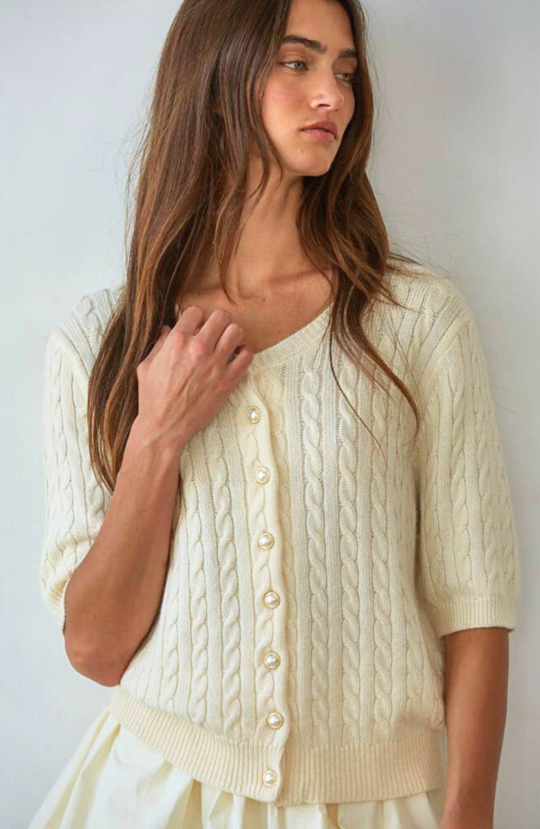Woman wearing a cream-colored cable knit cardigan against a plain background