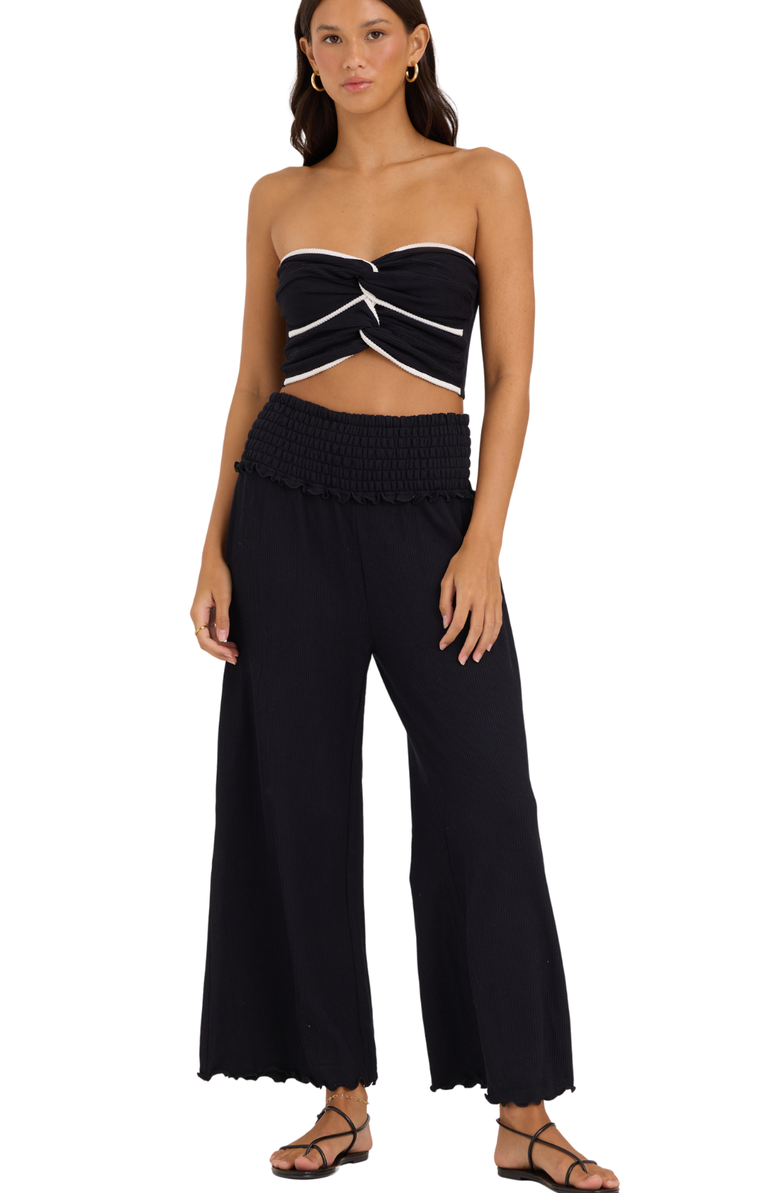 Woman wearing a black strapless top and wide-leg pants on a white background