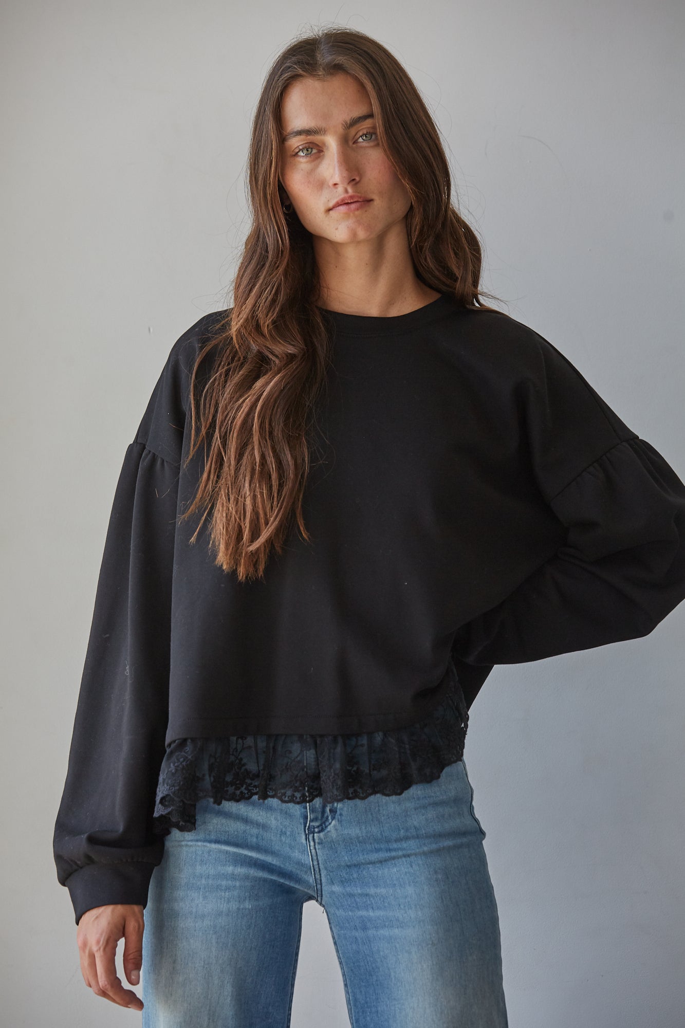 A woman modeling a black long-sleeve crewneck cotton sweatshirt with a lace hem, paired with wide-leg blue jeans.