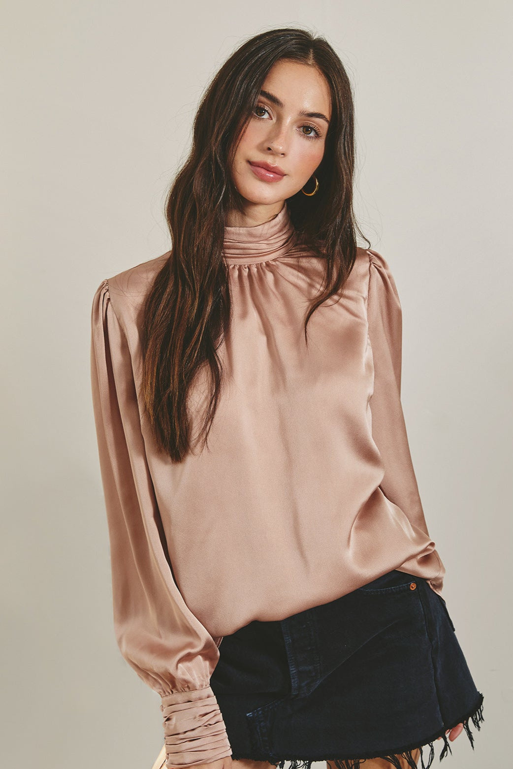 Woman wearing a satin blouse and denim skirt against a neutral background