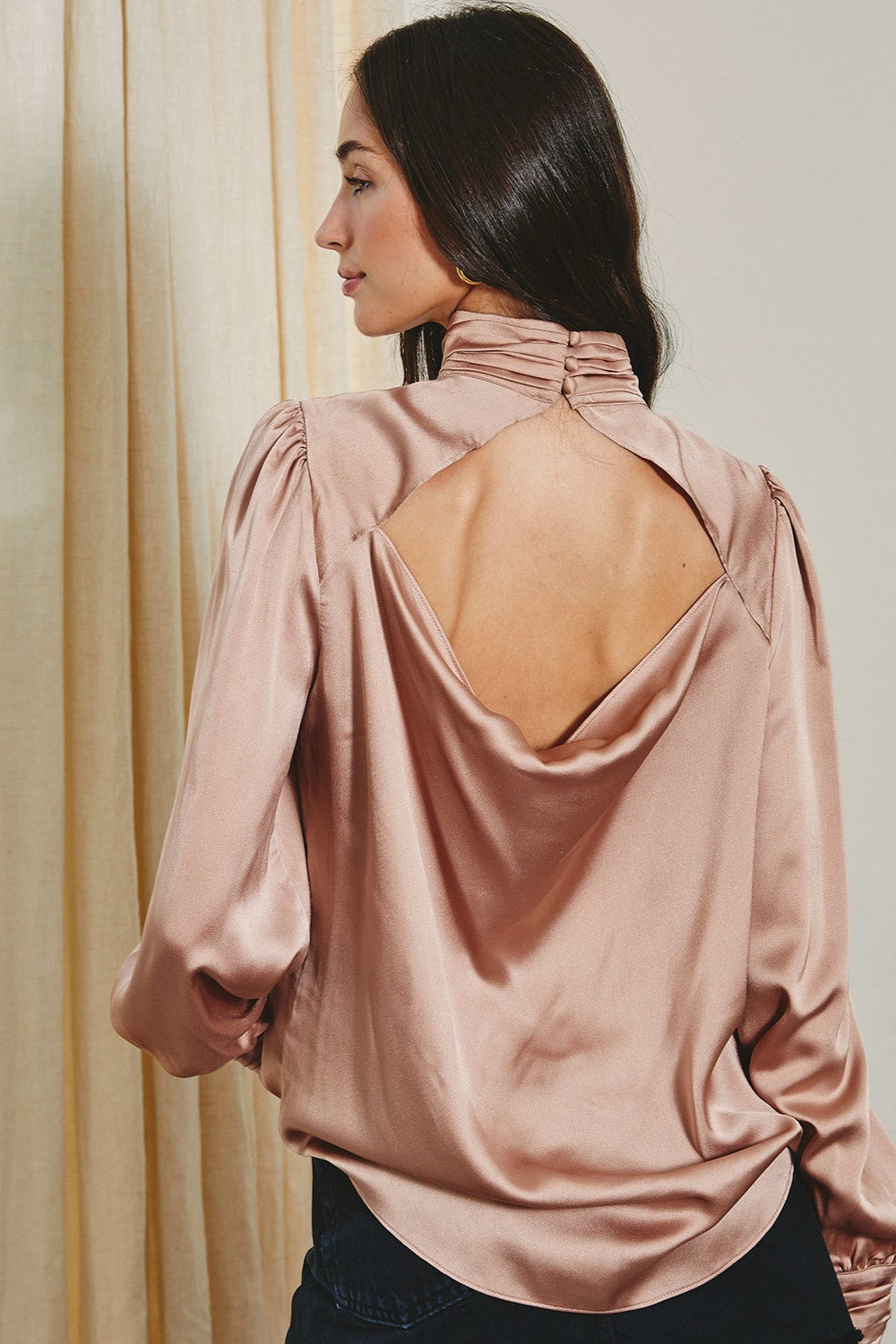 Woman wearing a pink satin blouse with a cut-out back design.
