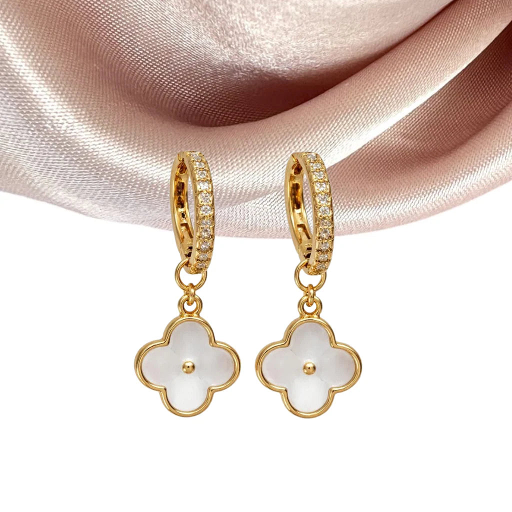 Gold hoop earrings with white mother of pearl clover charm on a pink satin background