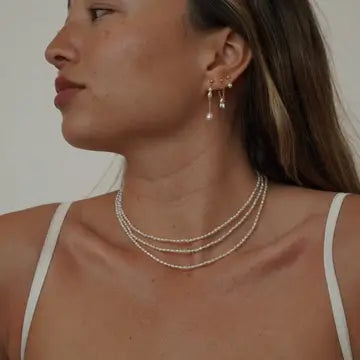 Woman wearing a pearl necklace and earrings against a neutral background
