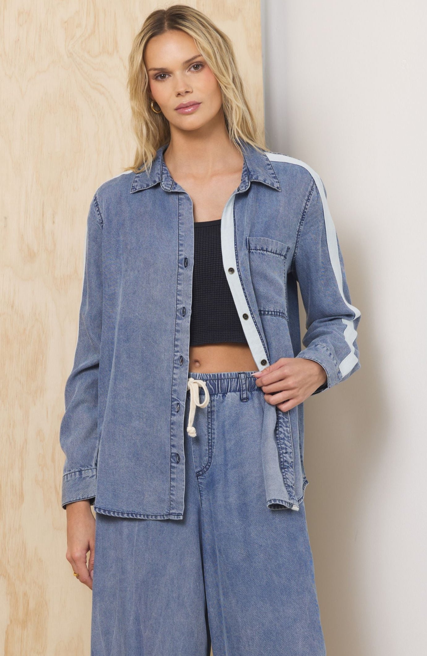 Woman wearing a denim outfit with wide-leg jeans and a matching jacket against a light-colored wall.