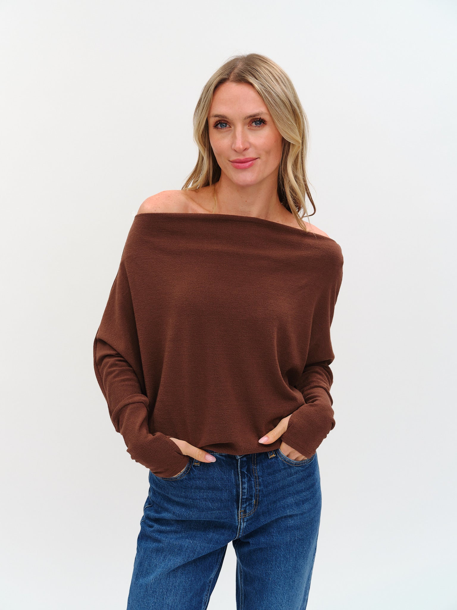 Woman wearing a brown off-shoulder sweater and blue jeans against a white background